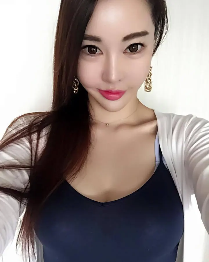 Femme asiatique aux cheveux longs, portant un haut bleu et une veste blanche, prenant un selfie.