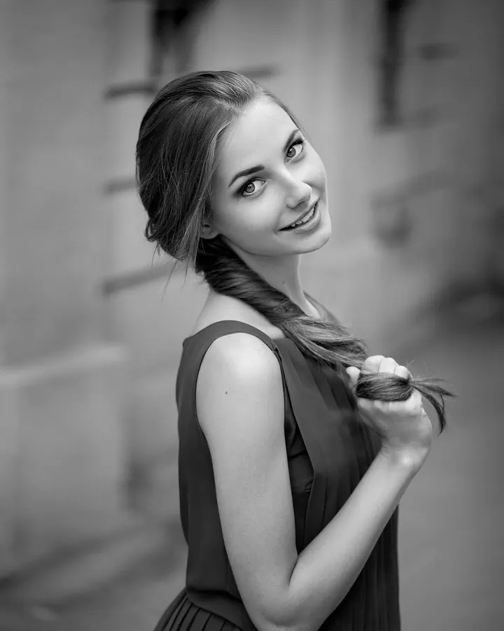 Jeune femme blonde, souriante, regardant l’objectif, cheveux attachés, dans une photo en noir et blanc.