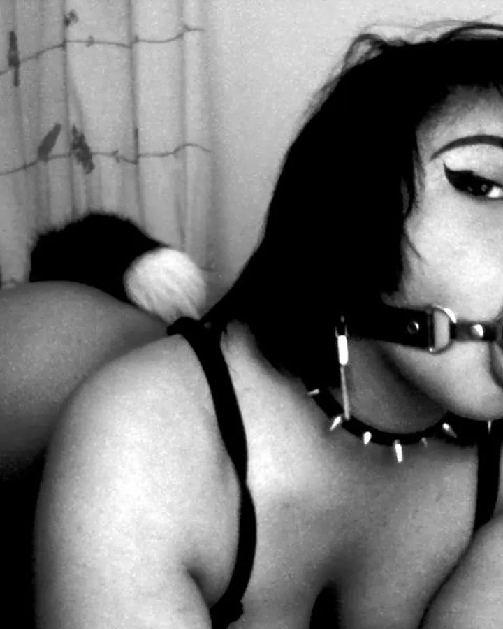 Femme noire en noir et blanc, bouche bâillonnée, collier à pointes, posture allongée