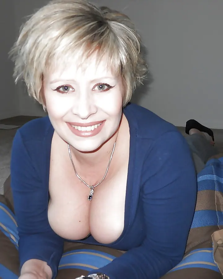Femme en tenue médicale bleue, assise sur une chaise dans une salle avec un badge autour du cou