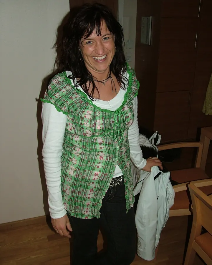 Femme souriante en chemisier vert, debout dans une pièce avec des cheveux noirs et un collier fin