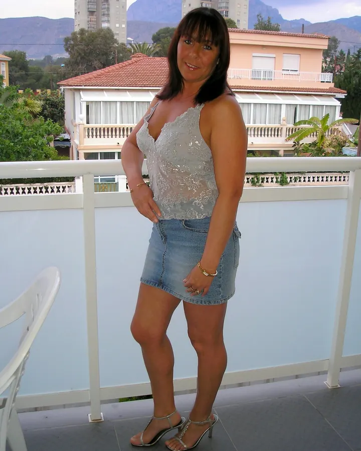 Femme en haut transparent argenté et jupe en jean, posant sur un balcon