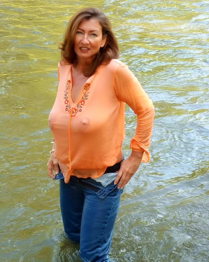 femme mature en jean et chemisier orange transparent, debout dans l’eau