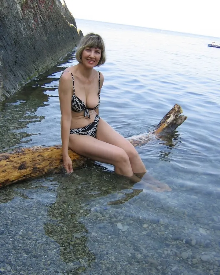 femme blonde en bikini rayé noir et blanc, assise sur bois dans l’eau