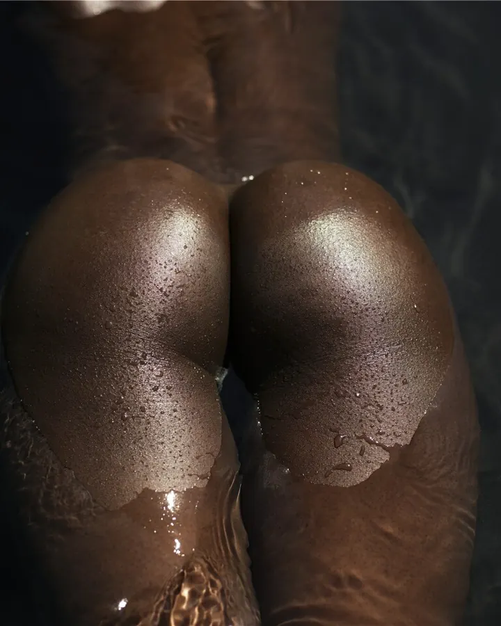 Fesses d'une femme noire émergeant de l'eau, la peau humide sous la lumière.