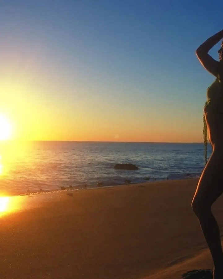 Silhouette féminine sur une plage au coucher du soleil, mains dans les cheveux