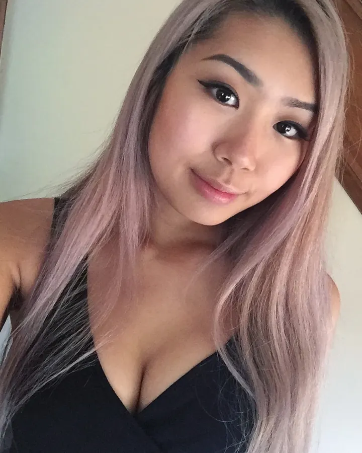 Portrait proche d’une jeune femme aux cheveux roses, souriante, en haut noir.