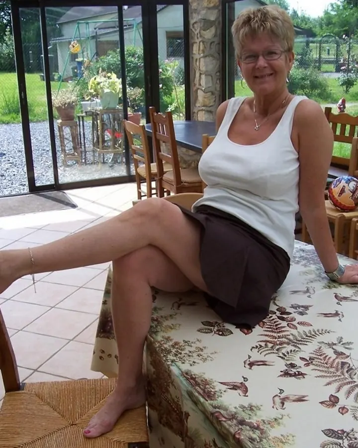 Femme aux cheveux blonds, portant un haut noir, assise sur un canapé, les pieds nus sur une table.