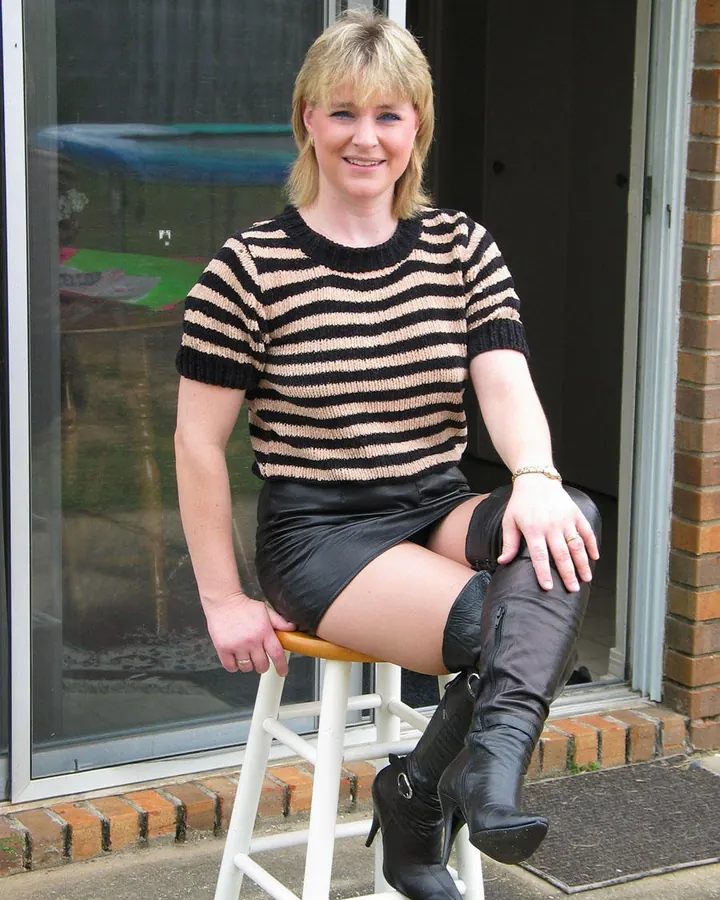 Femme aux cheveux blonds, portant un haut noir, assise sur un canapé, les pieds nus sur une table.