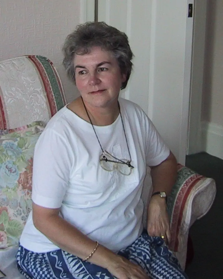 Femme aux cheveux gris, en tenue décontractée, posant dans un cadre intérieur.