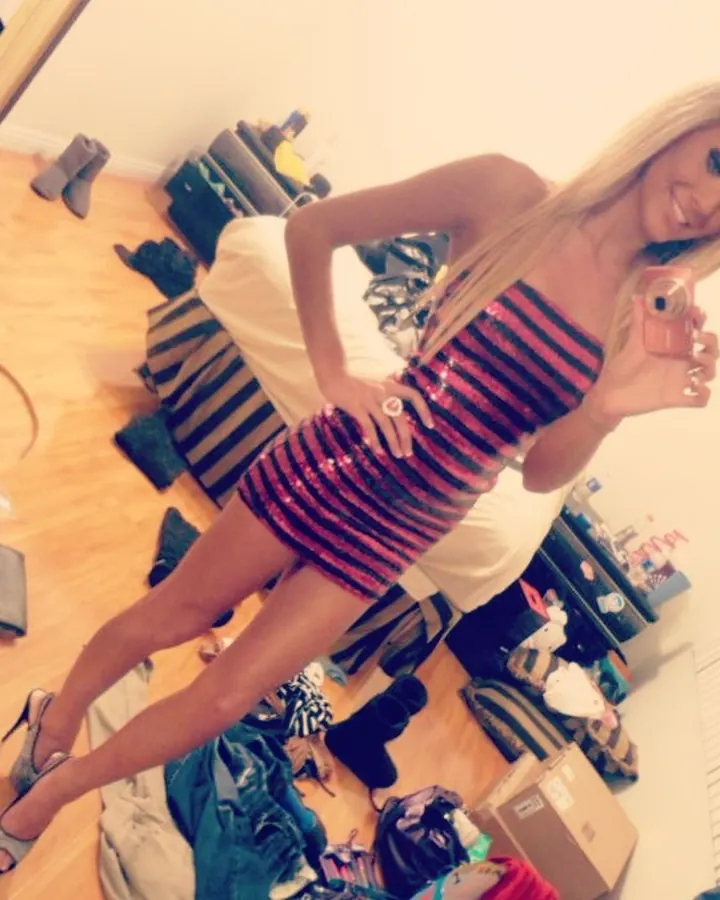 Jeune femme blonde, souriante, portant un collier à carreaux, assise à une table en bois.