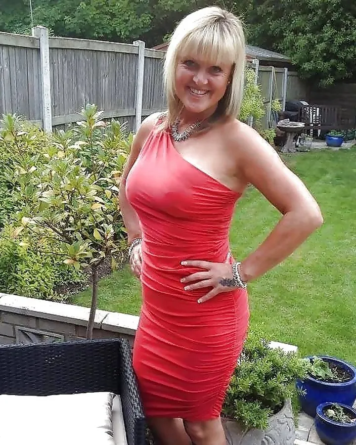 Femme blonde en robe rouge, posant dans un jardin